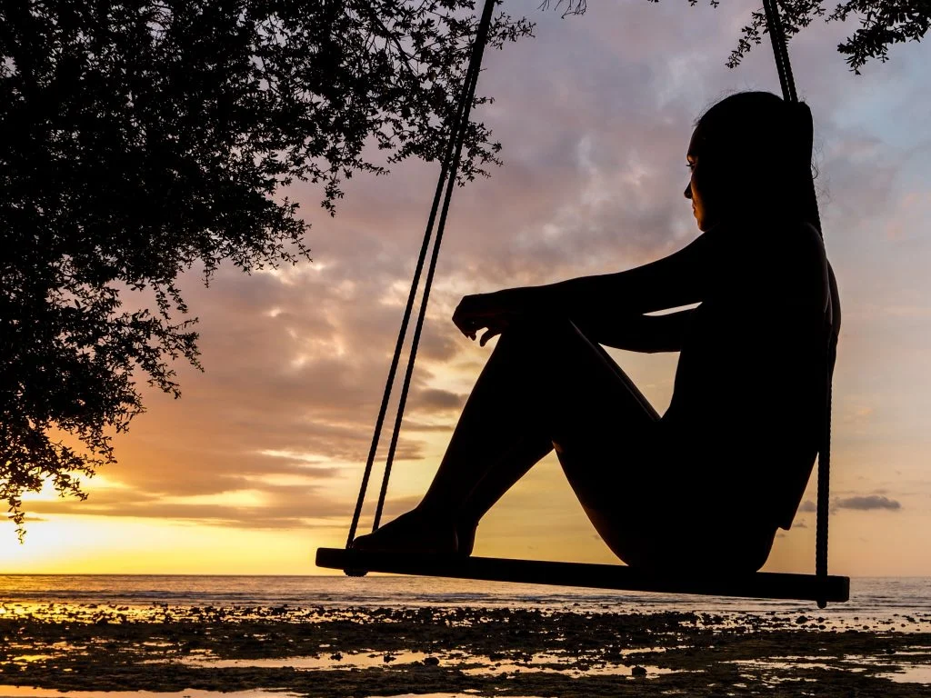 Man sitting on a swing at night watching over the city lights.