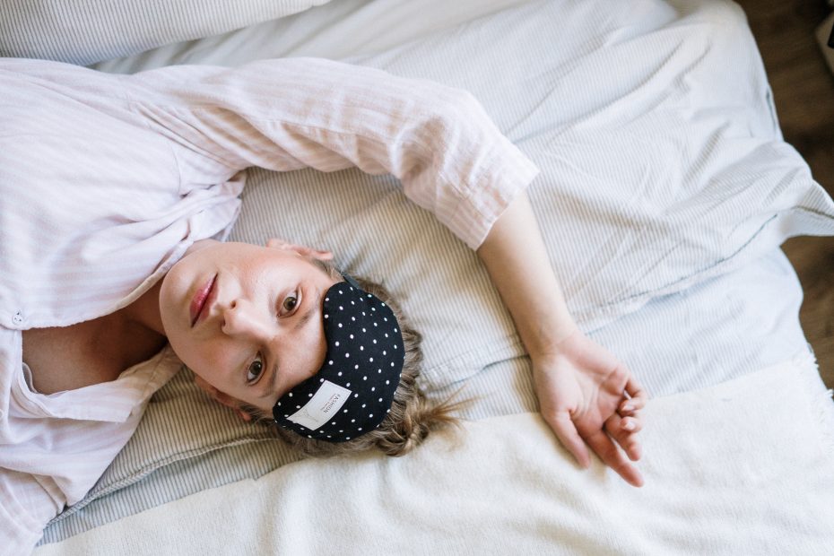 Woman laying on bed looking tired with a sleep eye mask