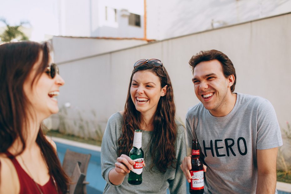 Woman and man holding a beer smiling while looking at another woman