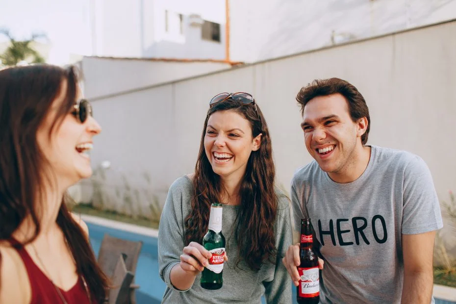 Woman and man holding a beer smiling while looking at another woman