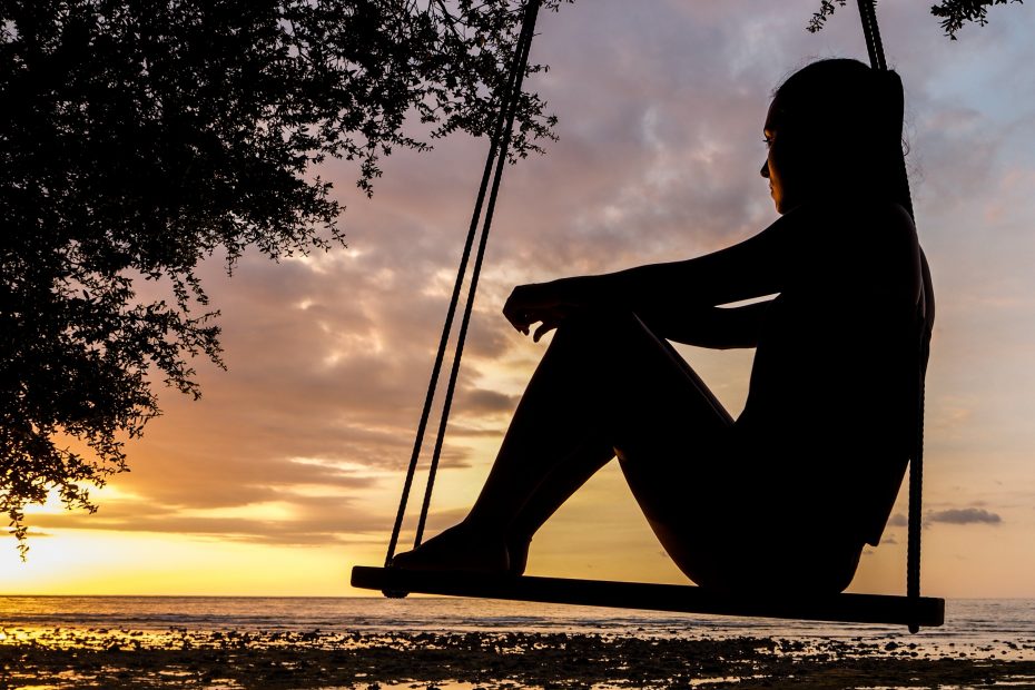 Man sitting on a swing at night watching over the city lights.