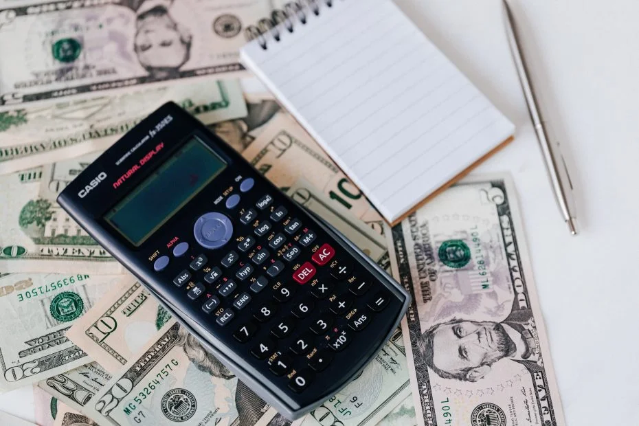 A calculator and notepad on top of a stack of dollar bills