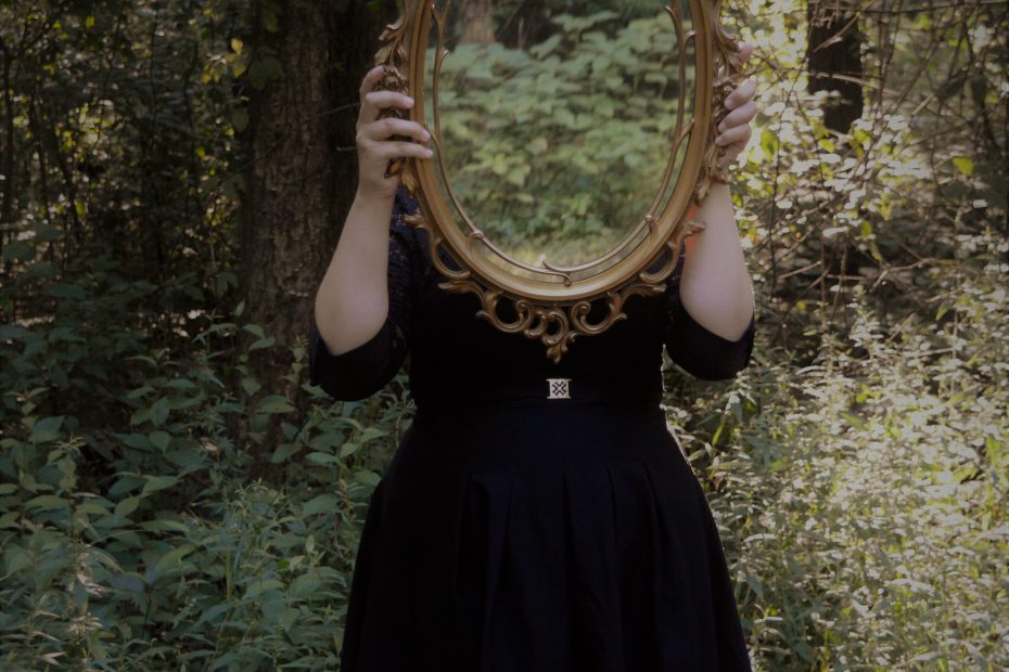 Woman in forest holding a mirror in front of her face