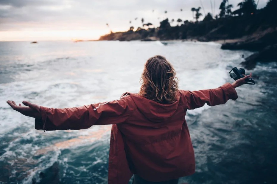 Woman standing by the ocean with her arms stretched out