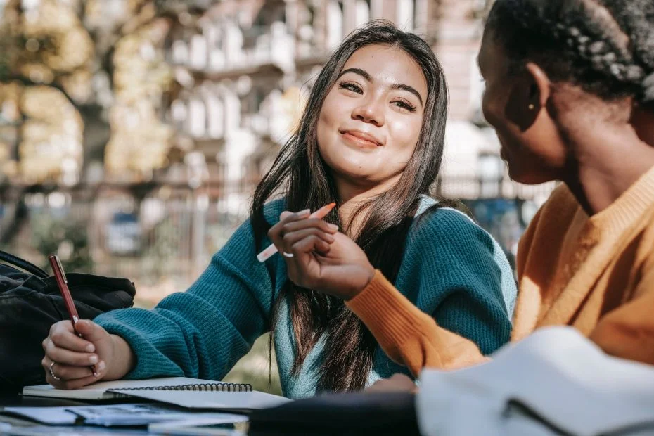 Two women smiling at each other while writing in notebooks