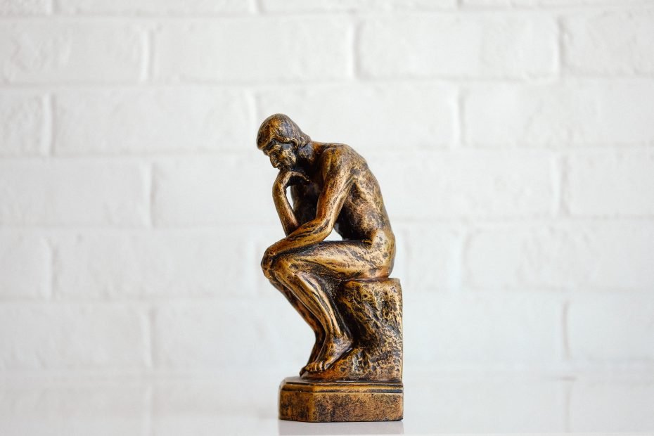 Thinking man statue in front of a white tile background